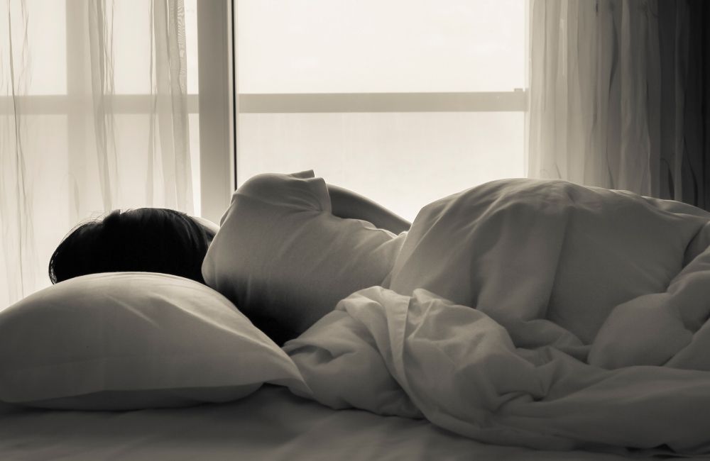 Eine Person liegt im Bett mit Blick Richtung Fenster