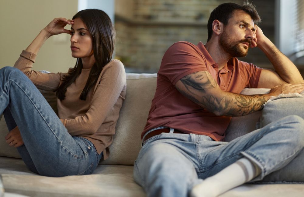 Eine Frau und ein Mann sitzen auf einem Sofa voneinander weggekehrt und sehen beide bedrückt aus