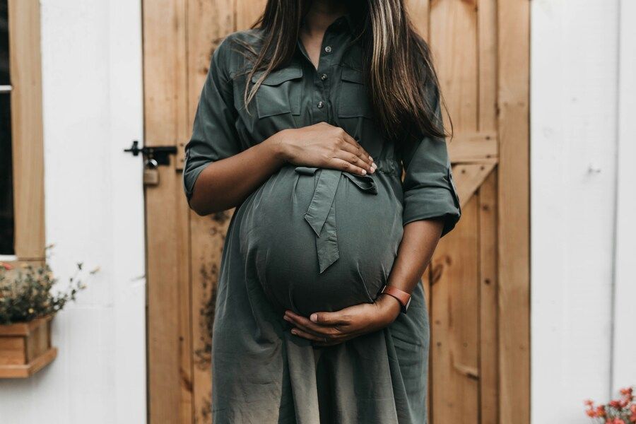 Eine schwangere Frau in einem dunkelgrünen Kleid hält sich den Babybauch.