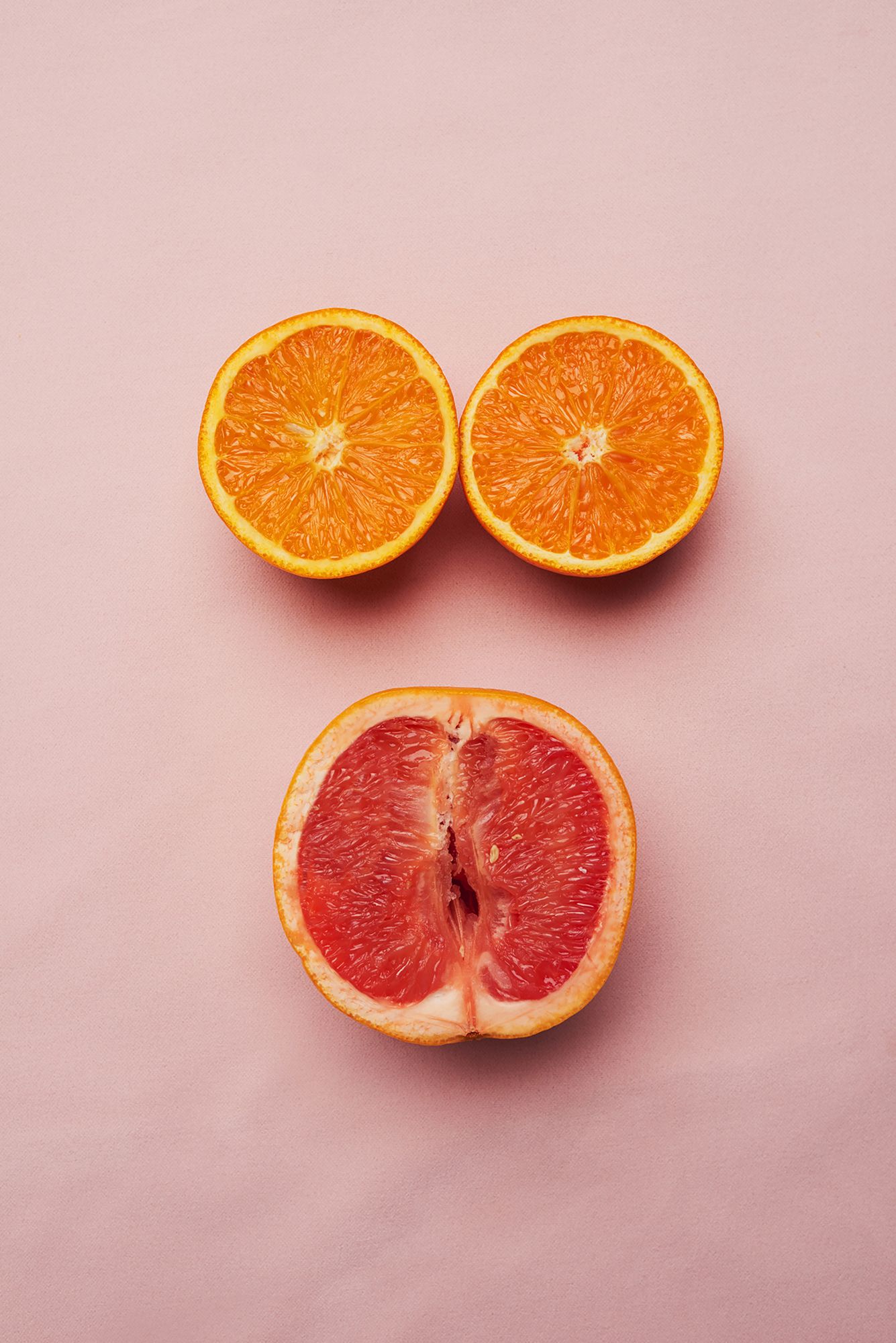 Aufgeschnittene Orange und halbe Grapefruit auf rosa Hintergrund