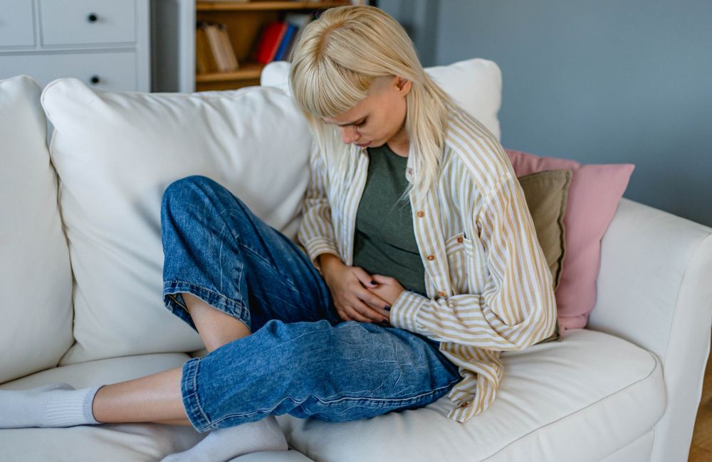 Eine Frau sitzt mit gesenktem Kopf auf dem Sofa und hält sich den Bauch