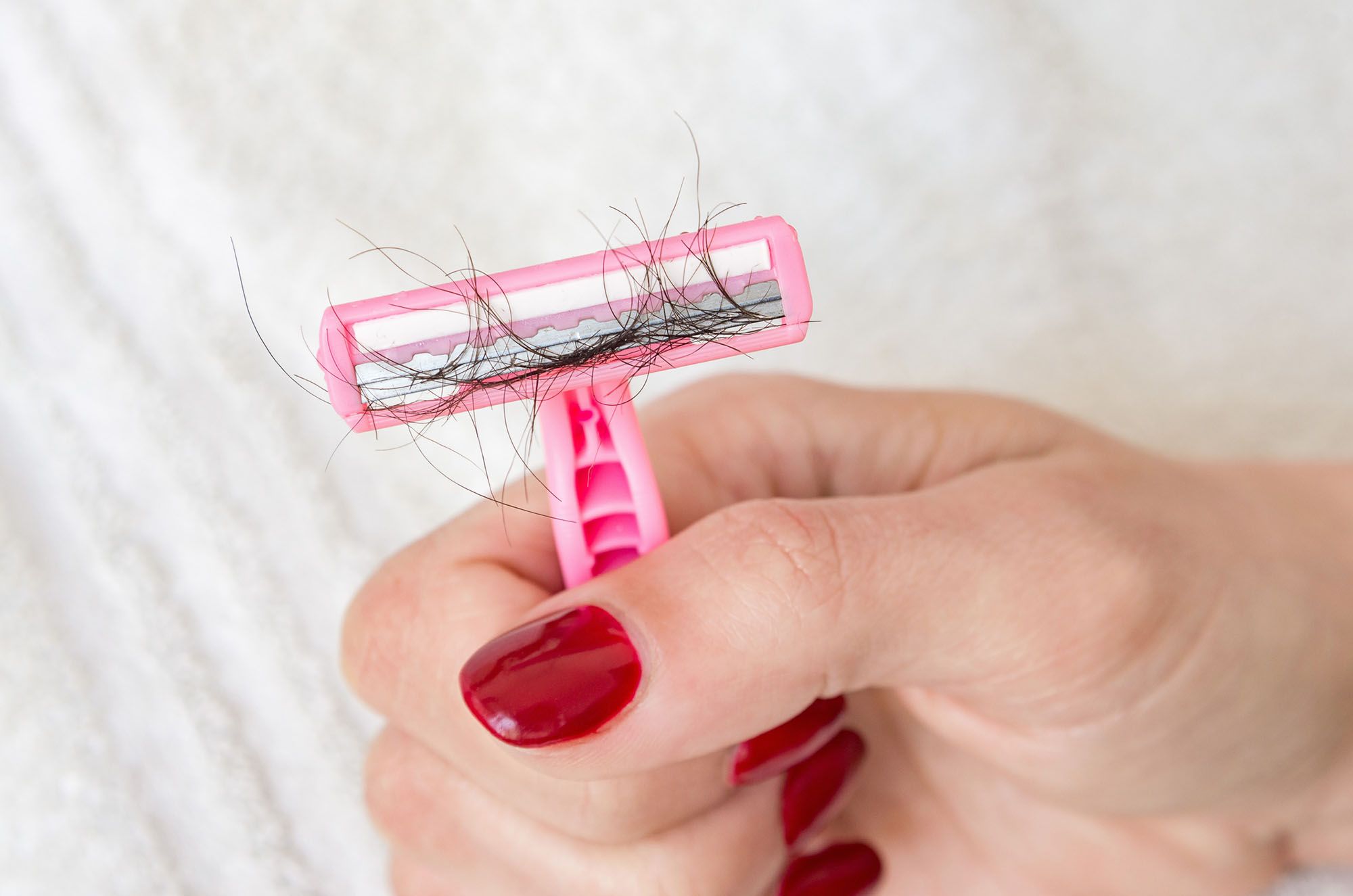 Rosa Rasierer mit schwarzen Haaren, der von einer Hand gehalten wird