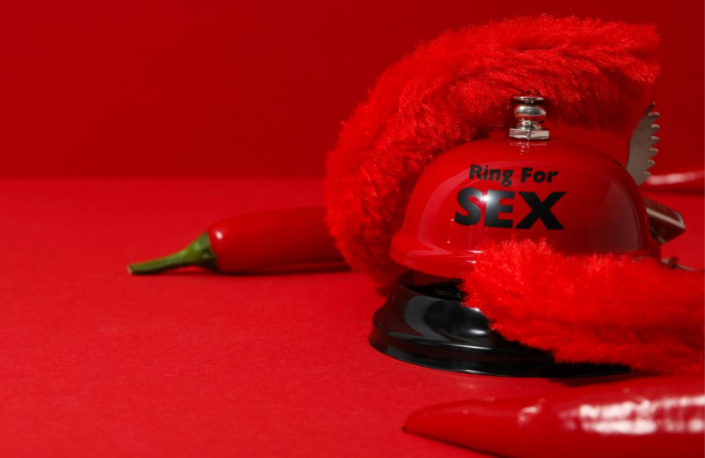 Eine rote Klingel, rote Plüschhandschuhe und eine rote Chillischote liegen vor einem roten Hintergrund.