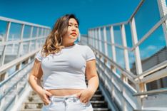 Kurvige Frau in Jeans und T-Shirt mit einer Treppe und blauem Himmel im Hintergrund