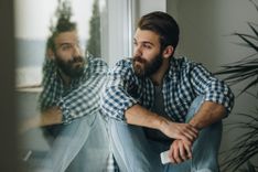 Mann sitzt nachdenklich mit Handy in der Hand am Fenster