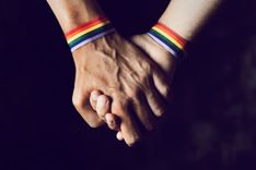 Zwei Hände, die sich gegenseitig halten und jeweils ein Armband in Regenbogenfarben tragen.