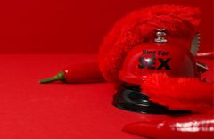 Eine rote Klingel, rote Plüschhandschuhe und eine rote Chillischote liegen vor einem roten Hintergrund.