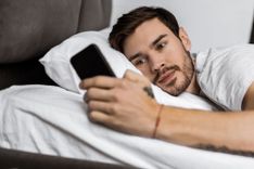 Mann liegt im Bett und schaut auf sein Handy