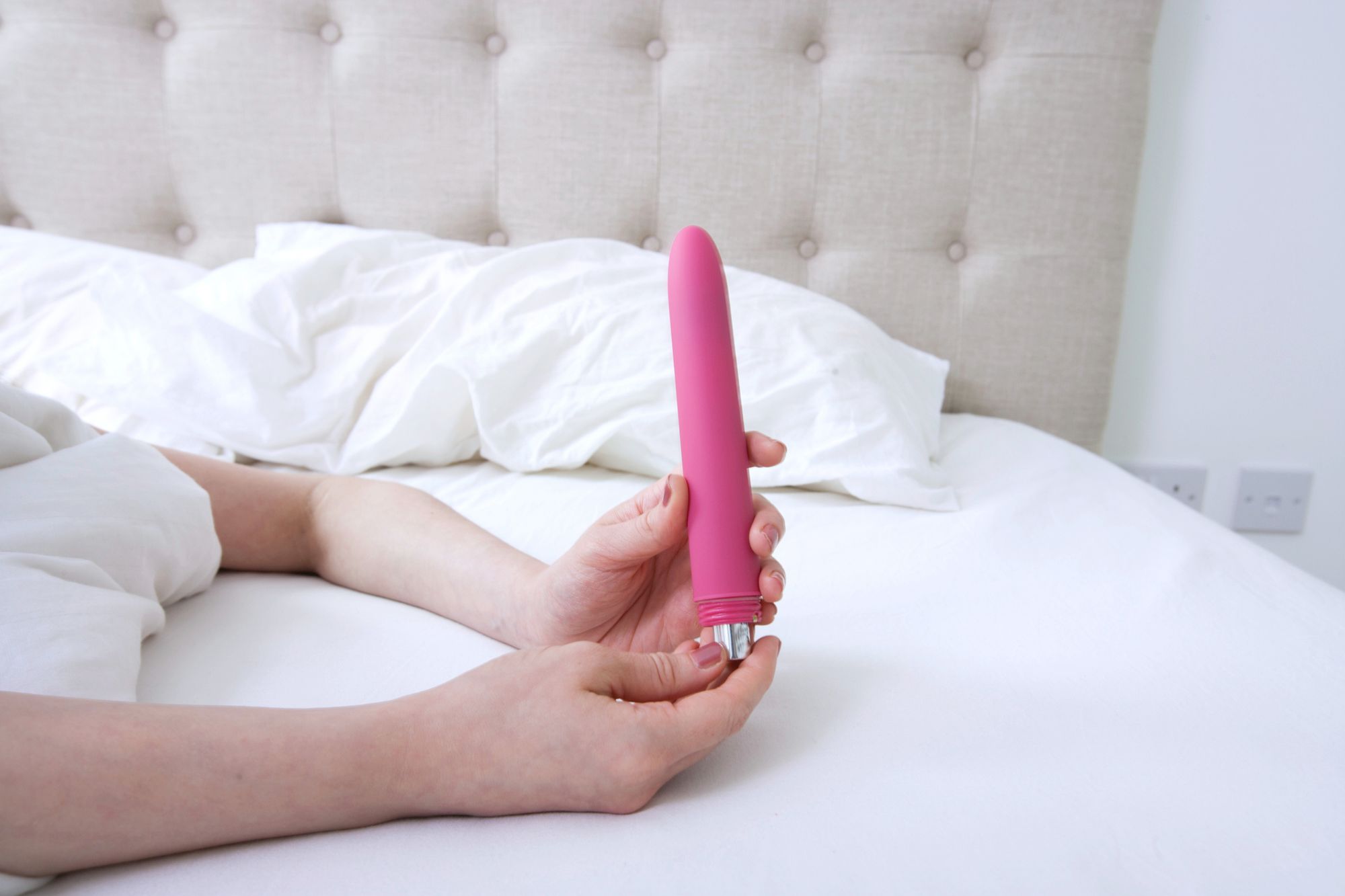 Zu sehen sind die Hände einer Person, die im Bett liegt und einen Vibrator in der Hand hält.