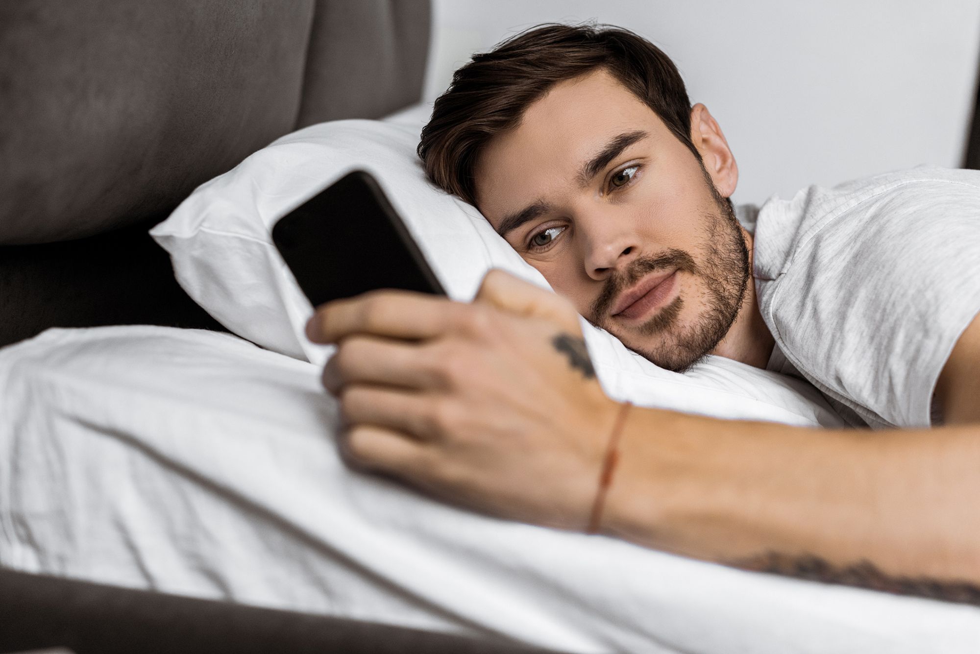 Mann liegt im Bett und schaut auf sein Handy